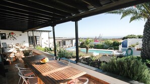 Un patio techado con una mesa y sillas de madera, una piscina y vistas al paisaje.