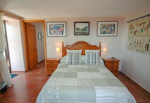 A bedroom with a large bed, two bedside tables with lamps, a wooden door, and three framed pictures on the wall.