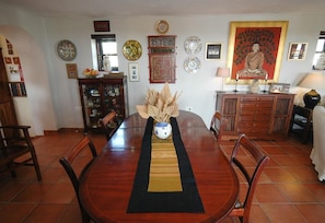 A dining area with a wooden table, chairs, a vase with dried plants, and a decorative wall with plates and a Buddha painting.