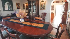 Un comedor con una mesa de madera, sillas, un florero con plantas secas y un armario con puertas de cristal.