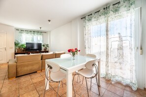 Una sala de estar con sofá, televisor, mesa de comedor, sillas y una ventana con cortinas de bambú.