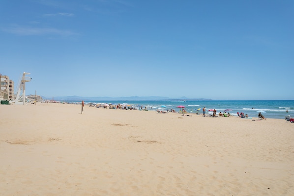 A beach with a clear sky, a few people, and umbrellas.