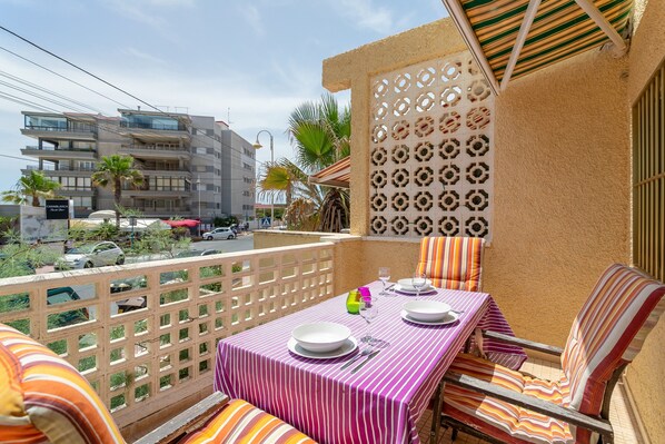 A balcony with a table set for two, a patterned wall, and a view of a building across the street.