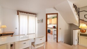 Une cuisine avec des meubles blancs, une table à manger avec des chaises et un escalier menant à l’étage supérieur.