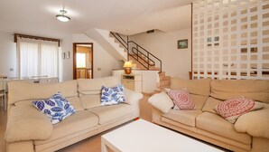 Un salon avec deux canapés beige, une table basse blanche, un escalier et une cloison blanche.