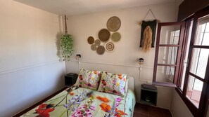 Quarto com colcha florida, planta pendente, decoração de parede e janela com vista.