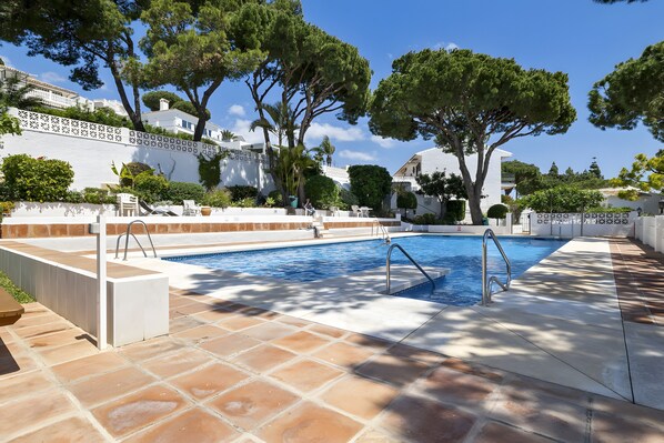 A swimming pool with a tiled deck, surrounded by white walls and trees.