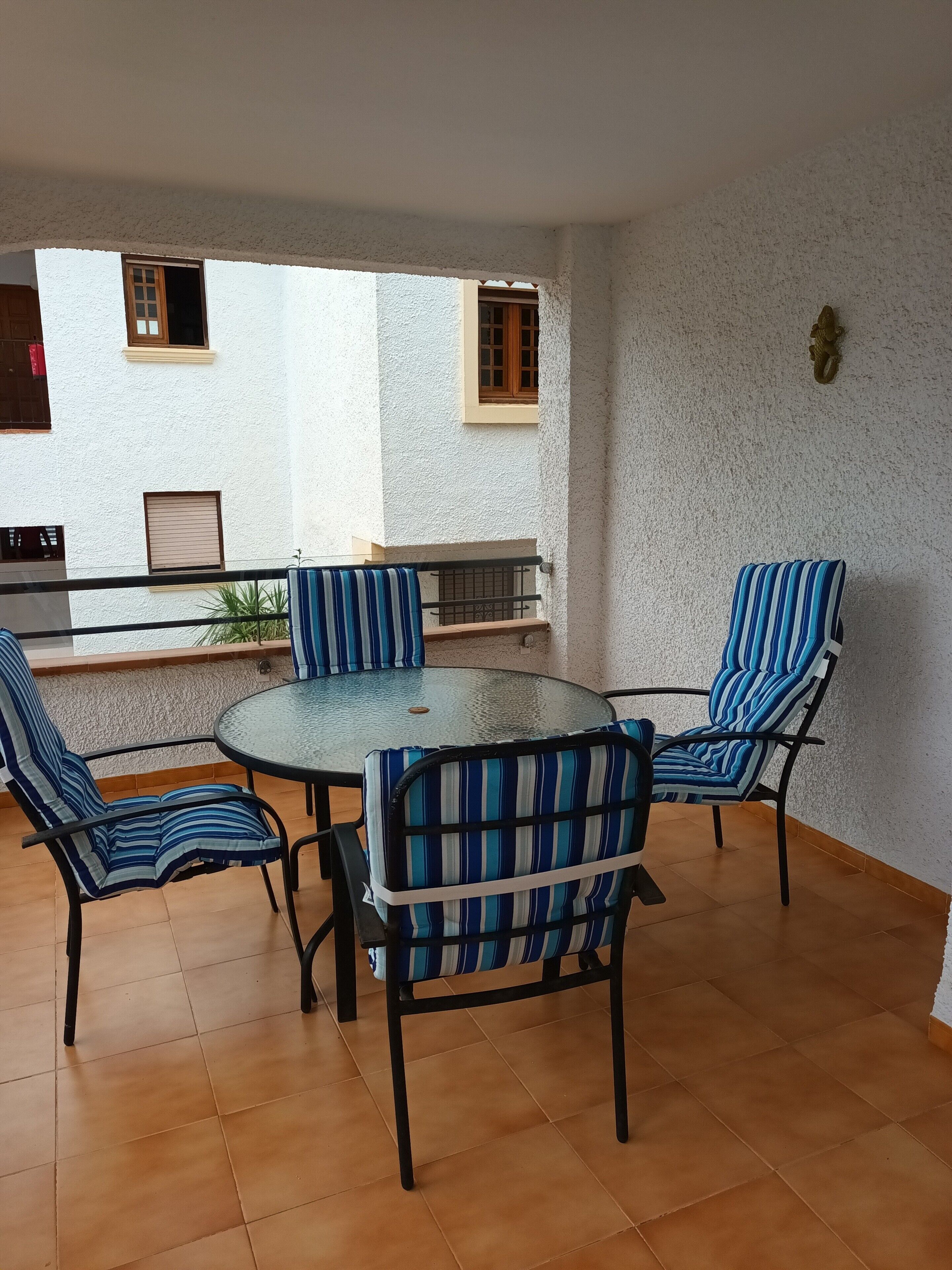 A dining area with a round glass table and four chairs with striped cushions.