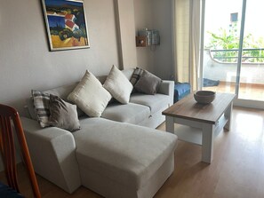 Un salon avec un canapé, des coussins, une table basse, un tableau accroché au mur et une vue à travers une porte vitrée.