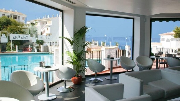Une chambre d’hôtel moderne avec vue sur la piscine, des meubles blancs et de grandes fenêtres.