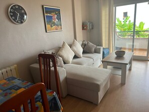 Un salon avec un canapé, une table à manger, une horloge et un tableau accroché au mur.