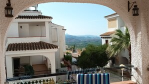 Un balcon avec vue sur des immeubles et des montagnes, une chaise à rayures et une table.