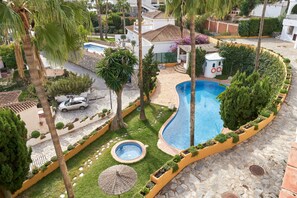 Un espace piscine doté d’un jacuzzi, de palmiers et d’un petit bâtiment avec une fenêtre circulaire.