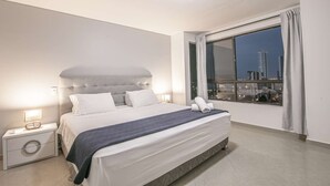 A modern hotel room with a large bed, a nightstand, a lamp, and a view of the city at night. - Luxury 8 Bedroom Penthouse with Private Jacuzzi (Cartagena)