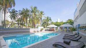 A swimming pool with lounge chairs, a covered seating area, and palm trees in the background. - Luxury 8 Bedroom Penthouse with Private Jacuzzi (Cartagena)