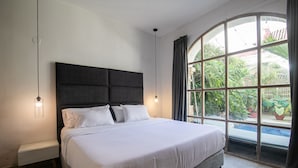 Een slaapkamer met een groot bed, een nachtkastje en een raam met uitzicht op een zwembad en groen.