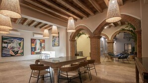 Un comedor espacioso con una larga mesa y sillas, rodeado de arcos de ladrillo y lámparas colgantes tejidas.