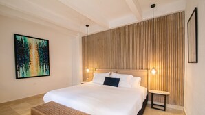 A modern hotel room with a large bed, a bedside table, a bench, a wall-mounted artwork, and a wooden panel wall.