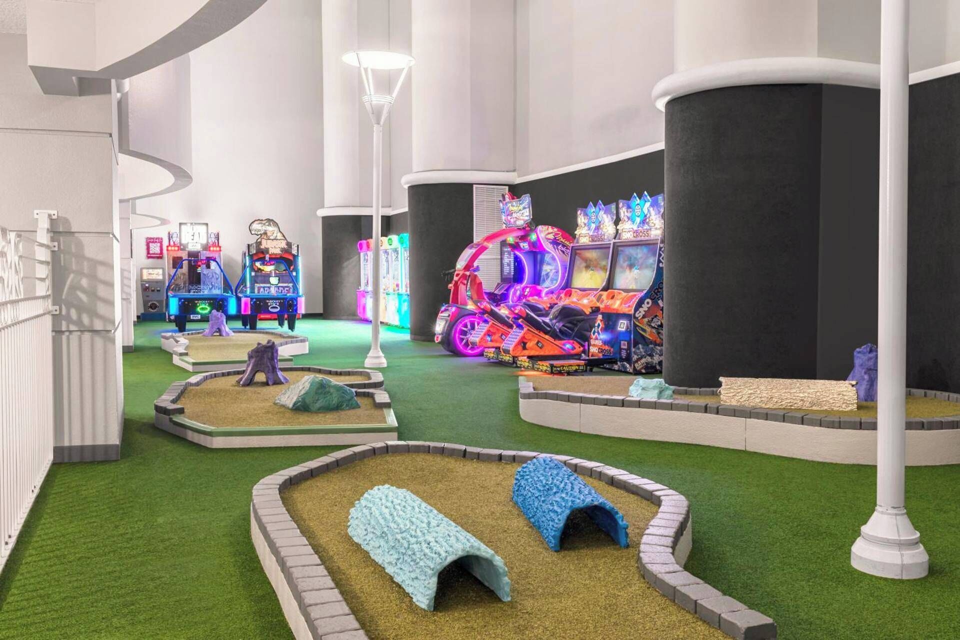 Un área de juegos interior con máquinas de arcade, un pequeño jardín con césped artificial y algunas bancas.