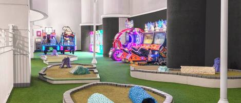 Un área de juegos interior con máquinas de arcade, un pequeño jardín con césped artificial y algunas bancas.
