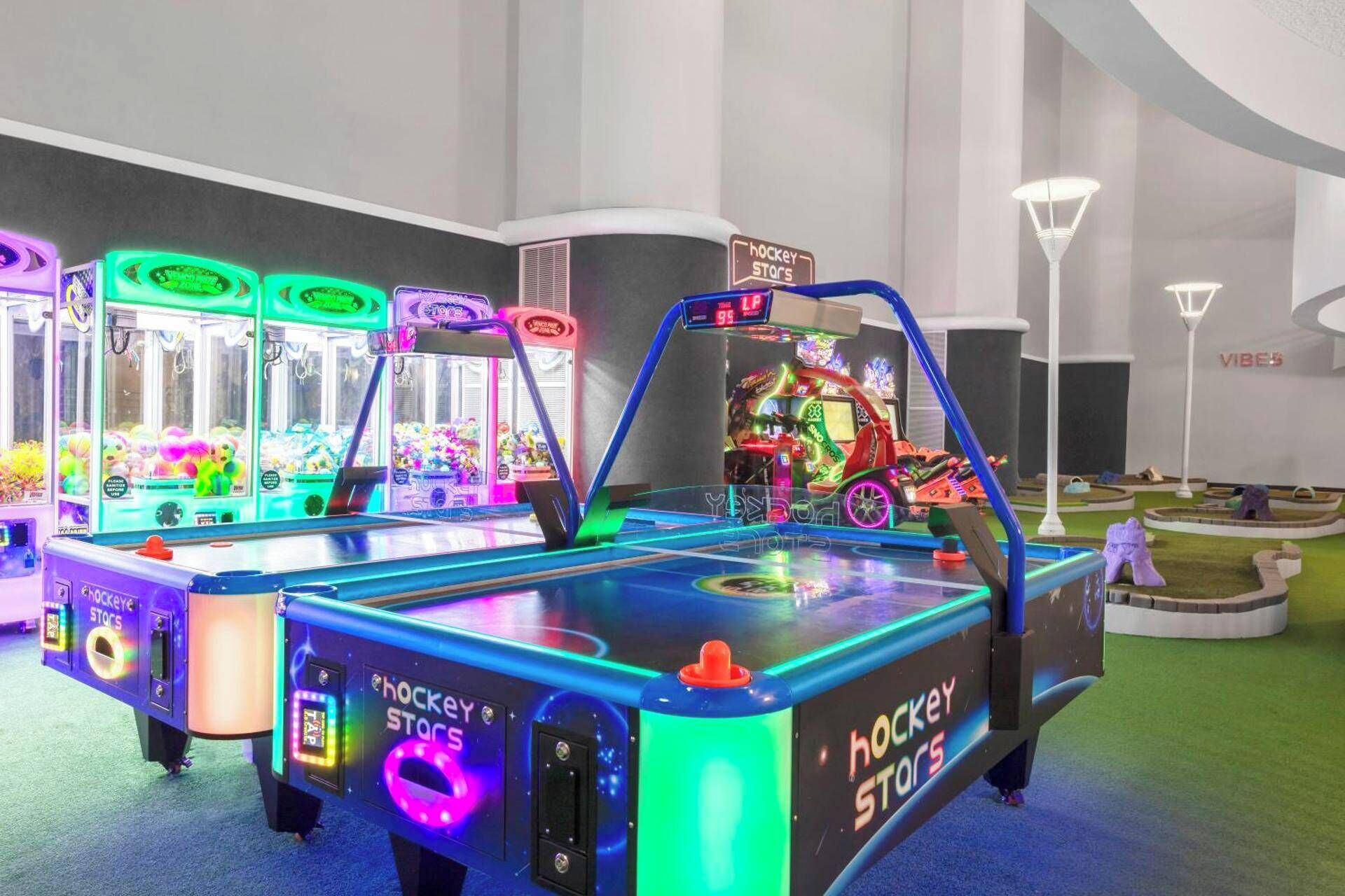 Un salón de juegos interior con varias máquinas de pinza y una zona temática de hockey.