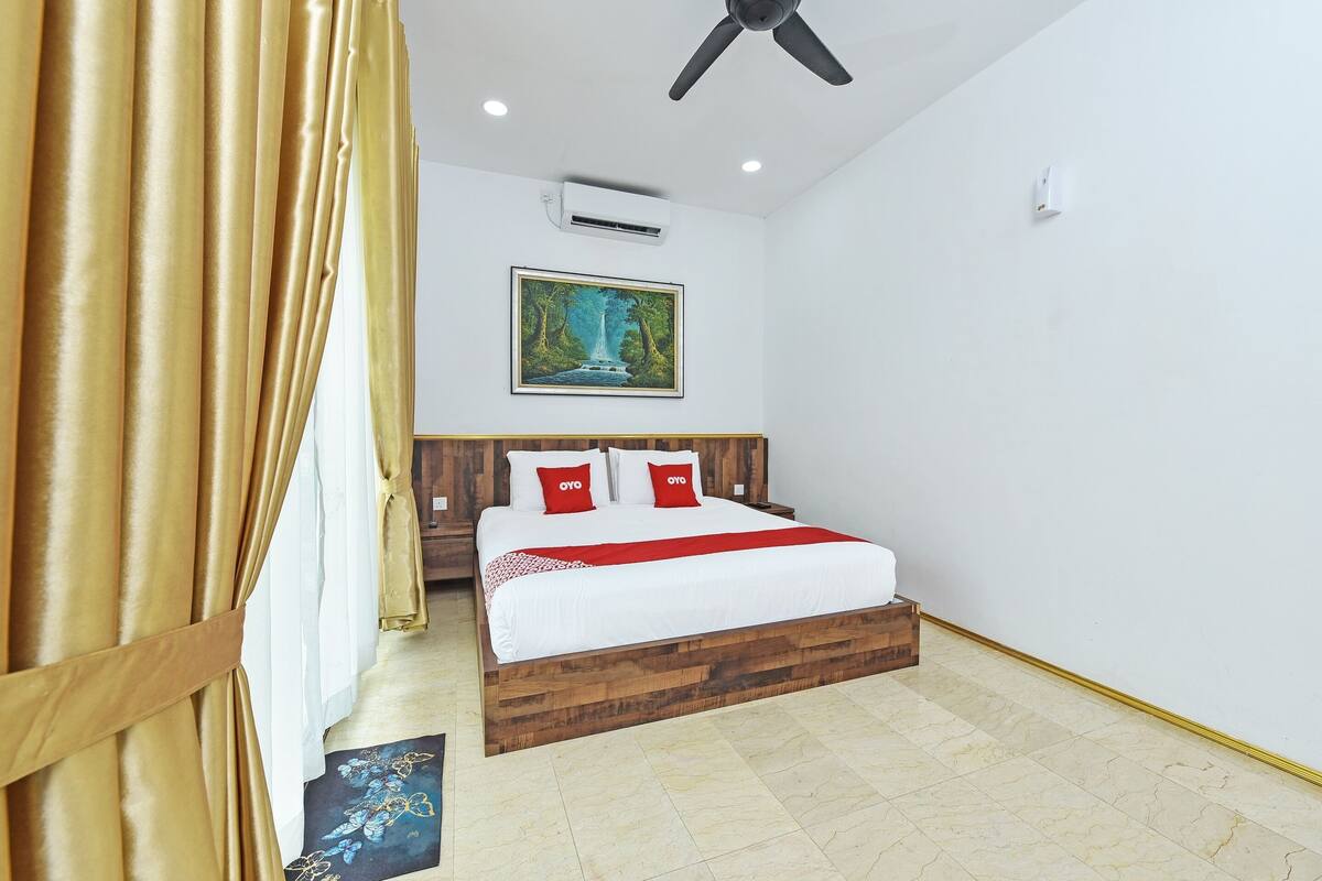 Een slaapkamer met een houten bed, wit beddengoed, rode kussens, een schilderij aan de muur en een airconditioning.