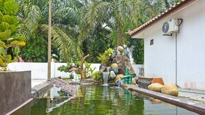 Un espace piscine extérieur paisible, agrémenté d’un élément aquatique, entouré d’une végétation luxuriante et bordé d’un bâtiment blanc.