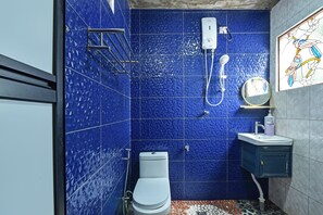A bathroom with blue tiled walls, a white toilet, a shower, and a small sink with a mirror.