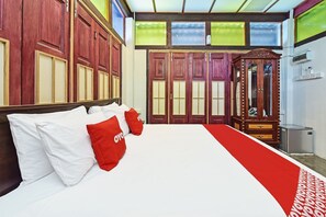 A hotel room with a large bed, red and white pillows, a wooden wardrobe, and a red carpet.