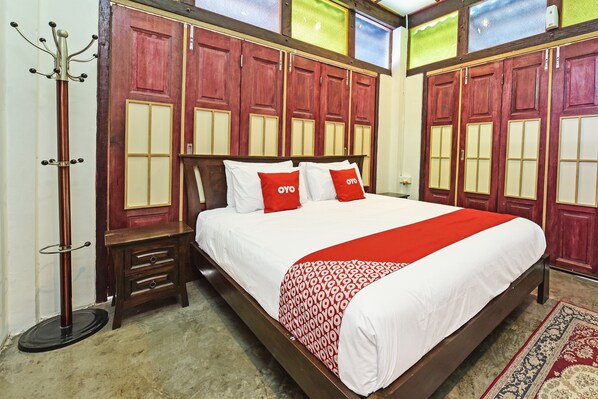 A hotel room with a large bed, wooden wardrobe, and a coat rack.
