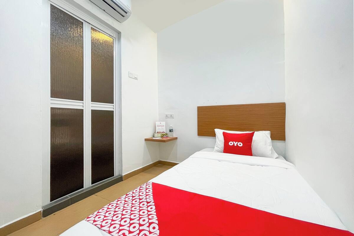 A hotel room with a bed, a wooden headboard, a red and white patterned throw, and a sliding glass door.