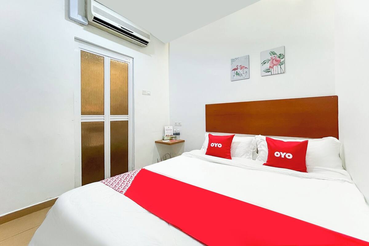 A hotel room with a bed, a nightstand, an air conditioning unit, and a sliding door.