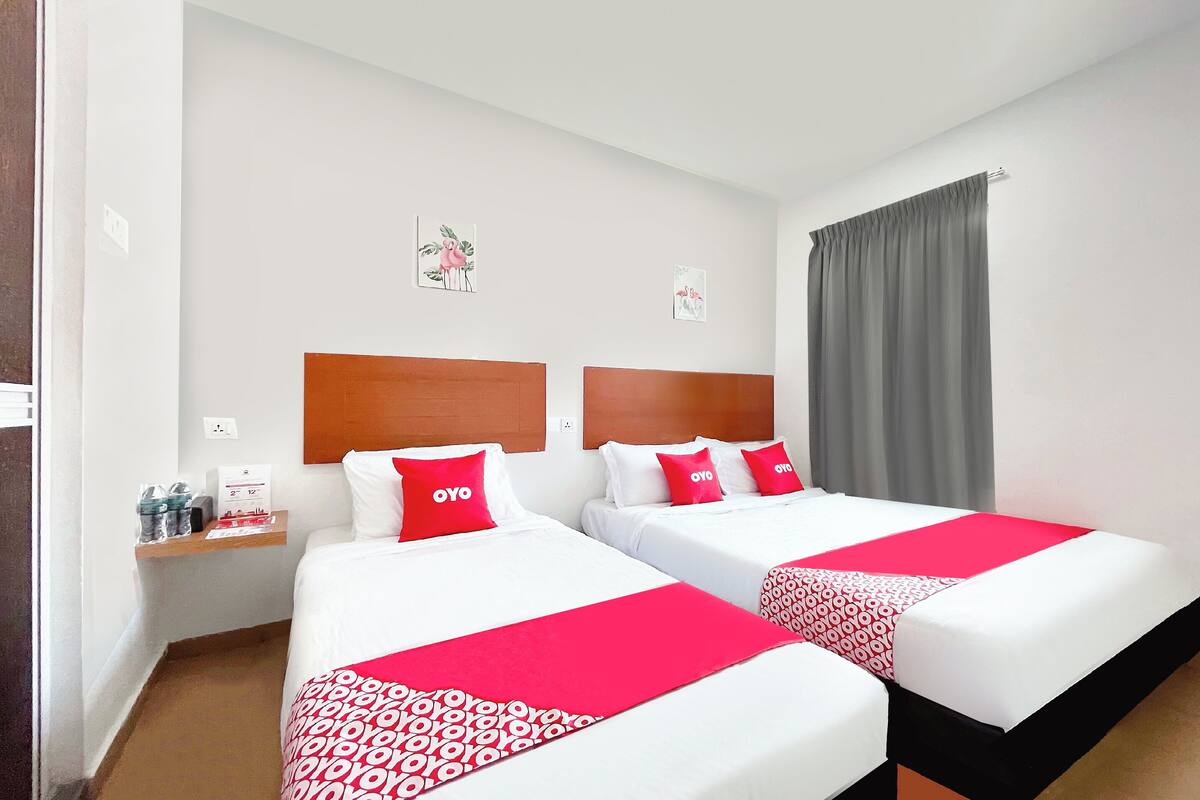 A hotel room with two beds, each with a red and white bedspread, and matching pillows. There is a small table with a water bottle and a tissue box.