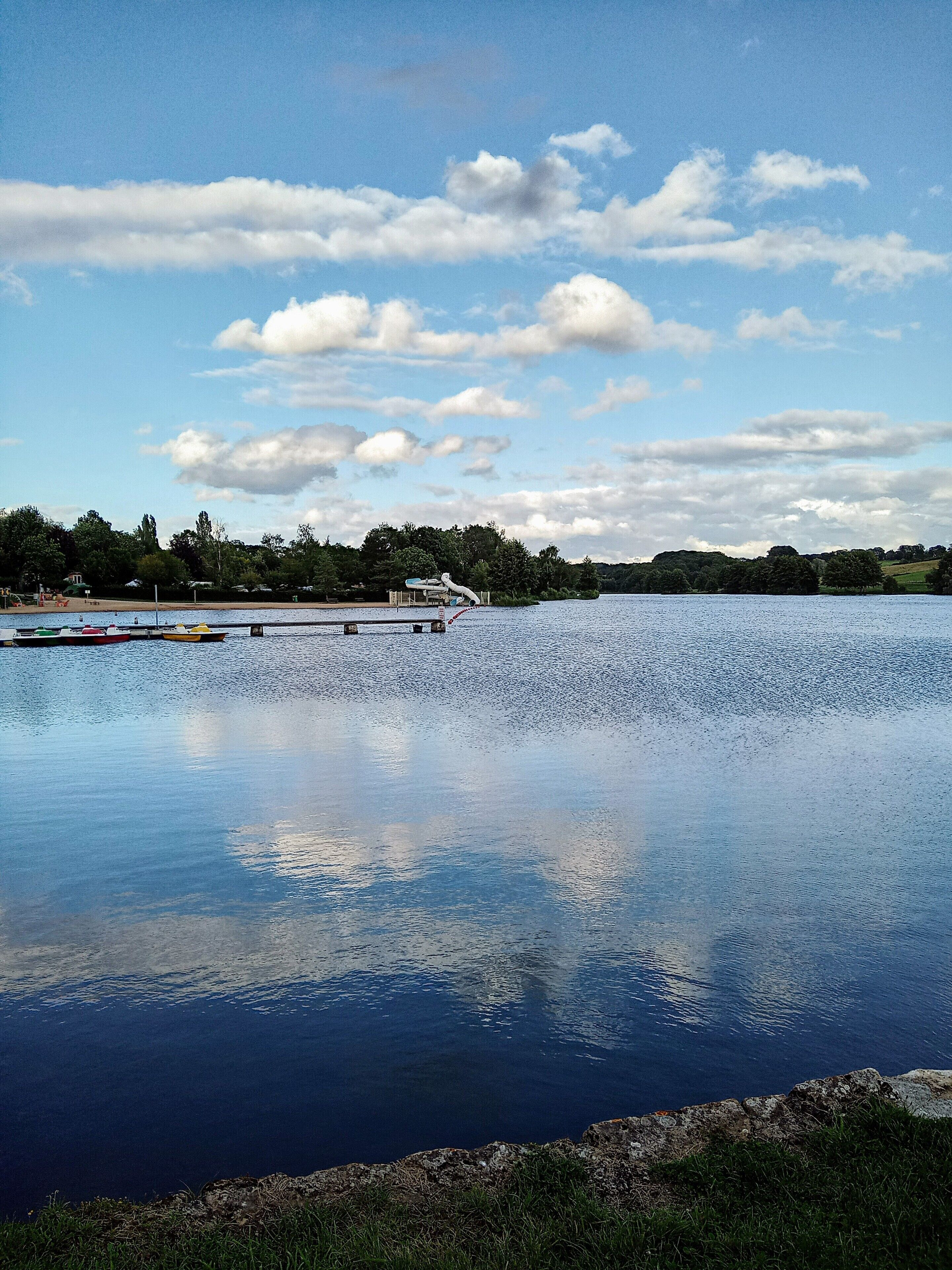 A calm lake with a dock and boats, surrounded by trees and a clear sky.