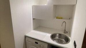 A compact kitchenette with a washing machine, a sink, and a small shelf.