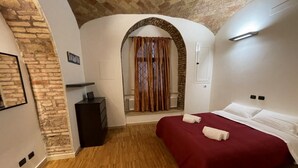A bedroom with a wooden floor, a red bedspread, and a brick wall.