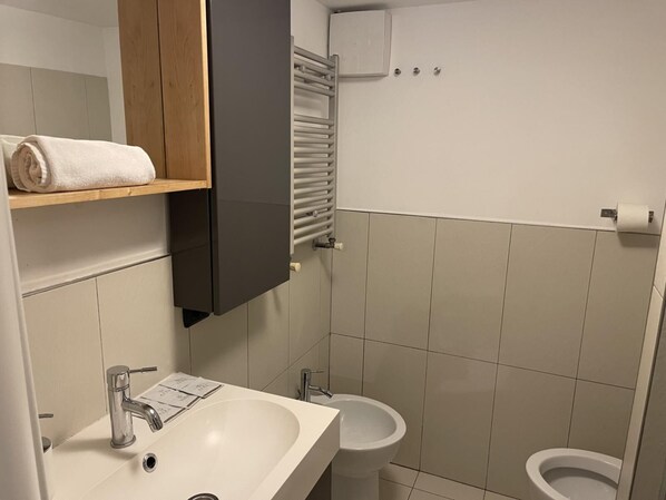 A bathroom with a sink, mirror, towel rack, toilet, and a towel on the rack. - San Lorenzo Guesthouse (Roma)