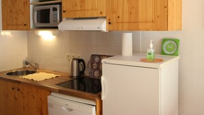 Uma cozinha compacta com armários de madeira, micro-ondas, chaleira, máquina de café, lava-louças e uma pequena geladeira.