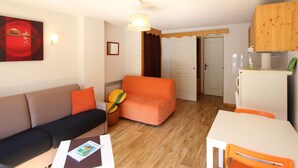 Um espaço de estar compacto com sofá, uma mesinha, uma mesa de jantar e uma cozinha.