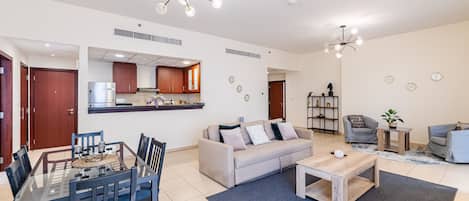 A modern living room with a sofa, coffee table, and dining area. There is a kitchen in the background with cabinets and a refrigerator.