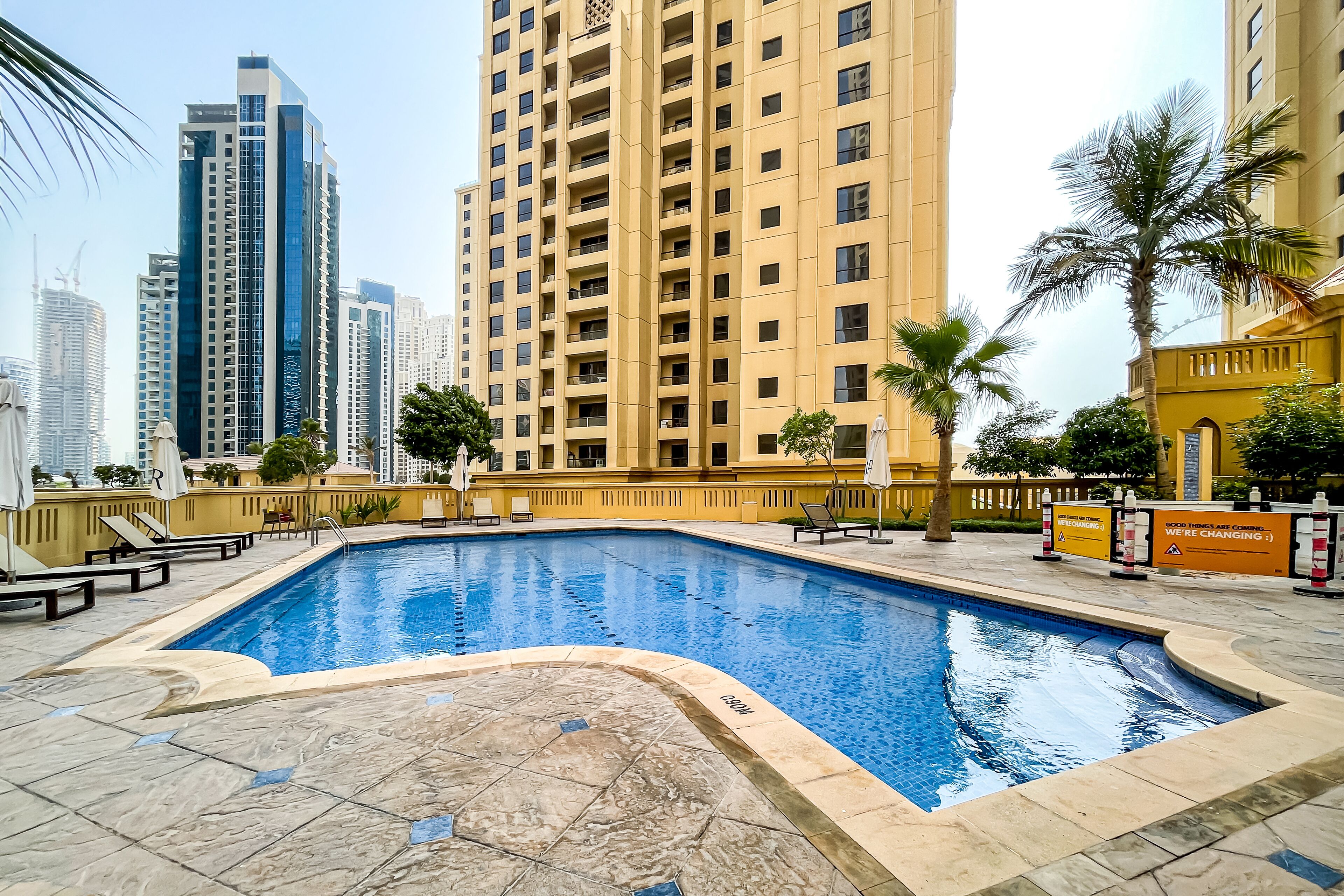 A swimming pool with a tiled deck, surrounded by high-rise buildings and palm trees.
