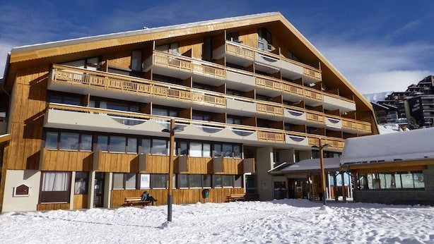 Ein mehrstöckiges Holzhaus mit Balkonen, verschneitem Untergrund und blauem Himmel.