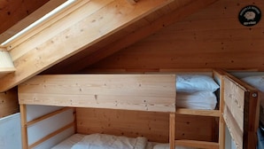 Ein Holzbett mit Etagen in einem Zimmer mit geneigter Decke und einem Oberlicht.