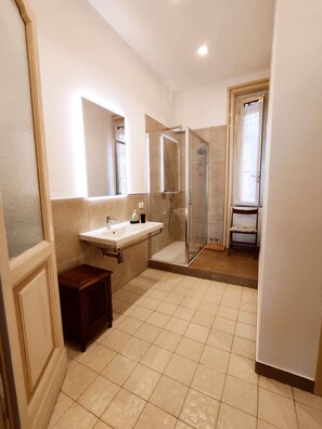 Bathroom features a large mirror, shower area with glass door, and a small stool.