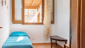 Ein kleiner Raum mit einem Bett, einem Fenster, einem Holztisch und einer Tür.