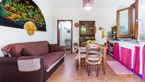 Ein Wohnzimmer mit Sofa, einem Esstisch und Stühlen, einer Küchenzeile mit Schränken und einem großen Gemälde an der Wand.