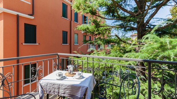 A balcony with a table set for two, surrounded by metal railings and a tree.