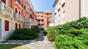 A courtyard with a paved walkway, green hedges, and multi-story buildings with balconies.