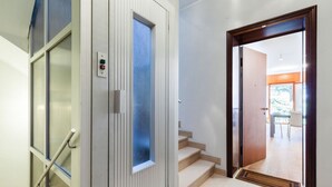 A modern interior with a glass door, a wooden door, and a staircase leading to a bright room with a view.