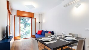 A modern dining area with a table set for two, a sofa with red cushions, and a TV on a stand.
